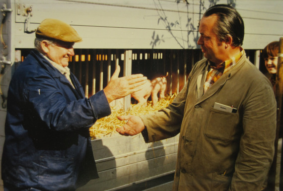 Zwei Männer stehen sich auf einem Schweinemarkt gegenüber. Sie stehen kurz vor einem Handschlag.