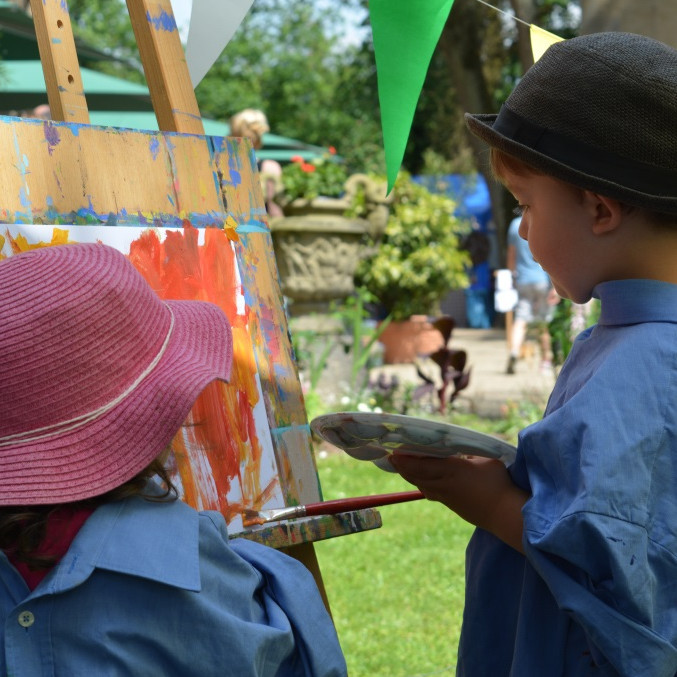 Ein Junge und ein Mädchen stehen vor einer Staffelei. Sie malen auf ein Papier.